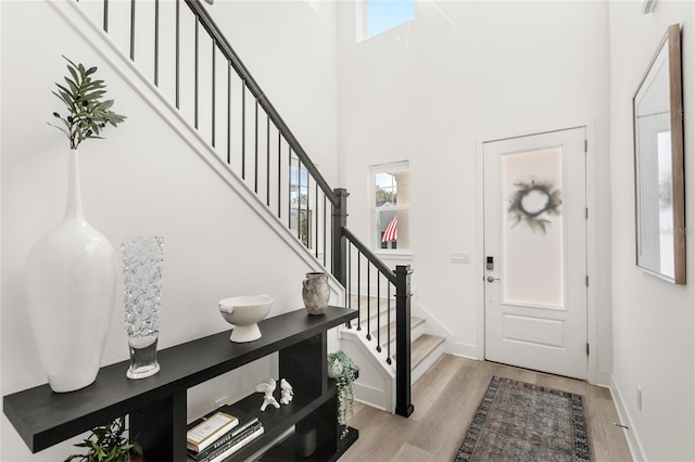 foyer entrance with stairs, baseboards, a towering ceiling, and light wood-style floors