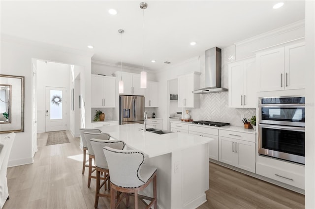 kitchen with crown molding, stainless steel appliances, a sink, wall chimney range hood, and a kitchen bar