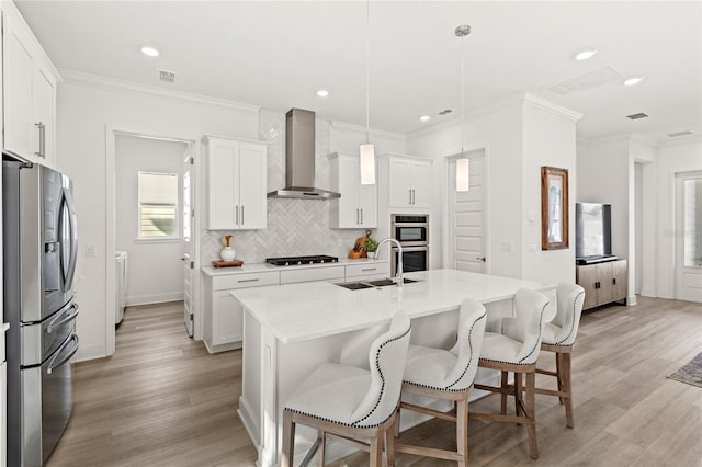 kitchen with a breakfast bar, stainless steel appliances, tasteful backsplash, a sink, and wall chimney exhaust hood