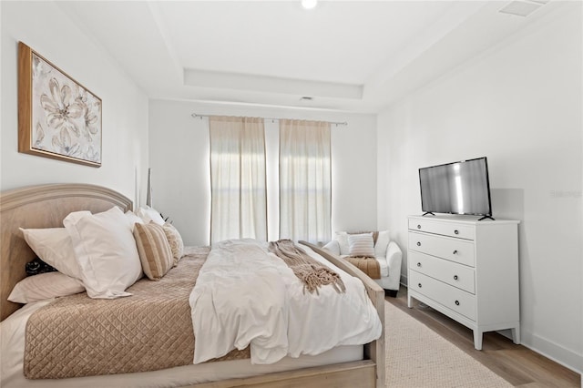 bedroom with baseboards, a raised ceiling, and wood finished floors