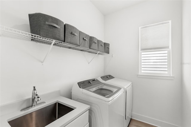 clothes washing area with laundry area, separate washer and dryer, a sink, and baseboards