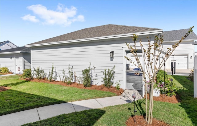 view of side of property featuring a shingled roof and a yard