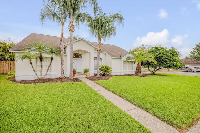 view of front of home featuring roof with shingles, fence, a front lawn, and stucco siding