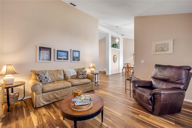 living room with high vaulted ceiling, wood finished floors, visible vents, and baseboards