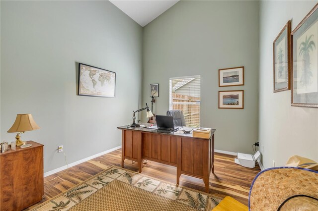office area featuring high vaulted ceiling, light wood-type flooring, and baseboards