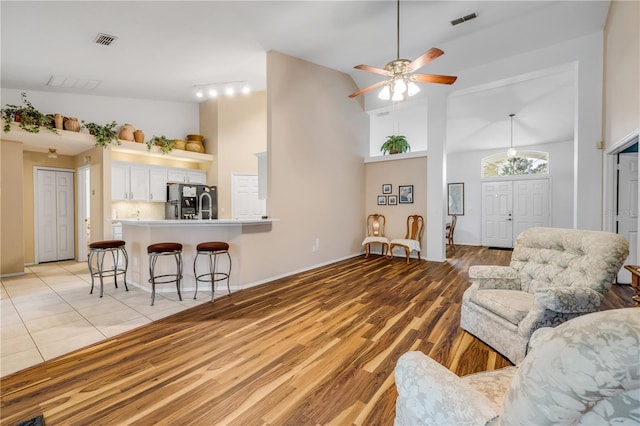 living room featuring high vaulted ceiling, visible vents, ceiling fan, and light wood finished floors