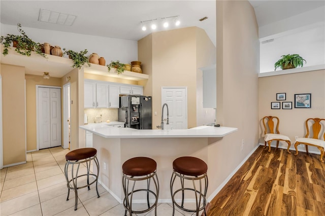 kitchen featuring light countertops, visible vents, white cabinets, a kitchen breakfast bar, and black fridge
