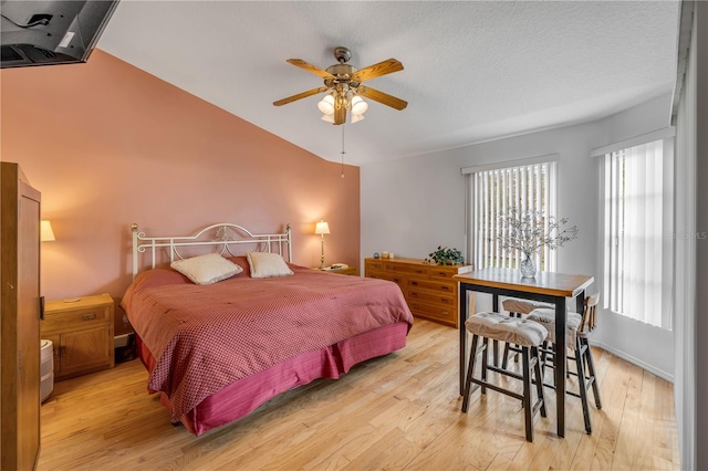 bedroom with baseboards, lofted ceiling, ceiling fan, a textured ceiling, and light wood-style floors