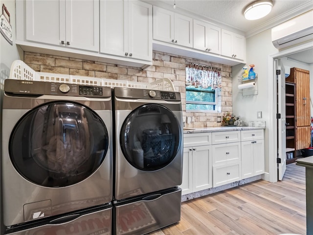 clothes washing area featuring cabinet space, washer and clothes dryer, light wood-style flooring, a wall mounted air conditioner, and crown molding