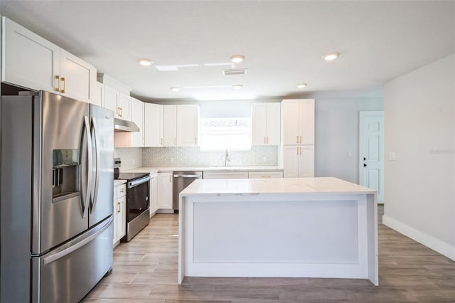 kitchen featuring a kitchen island, under cabinet range hood, decorative backsplash, stainless steel appliances, and white cabinetry