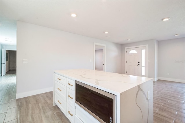 kitchen featuring a center island, light wood-type flooring, light stone counters, recessed lighting, and white cabinets