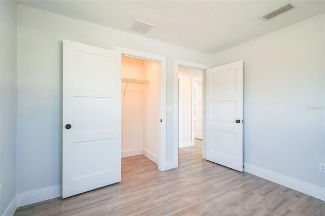 unfurnished bedroom with visible vents, light wood-style flooring, and baseboards