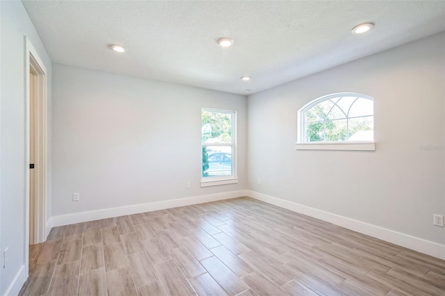 unfurnished room with recessed lighting, a textured ceiling, light wood-style floors, and baseboards