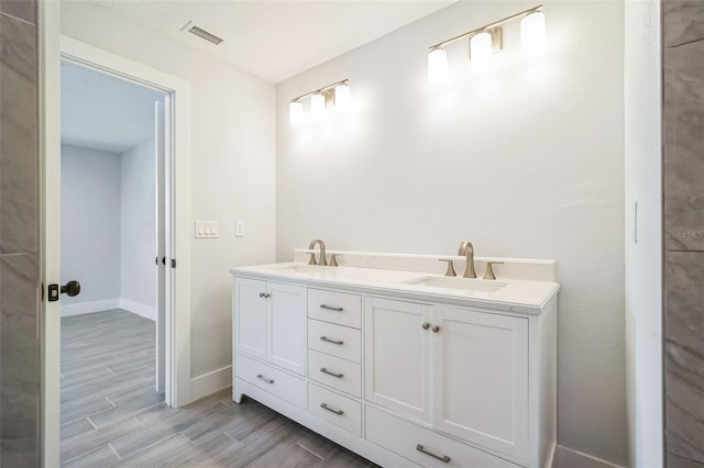 bathroom with a sink, baseboards, wood finish floors, and visible vents