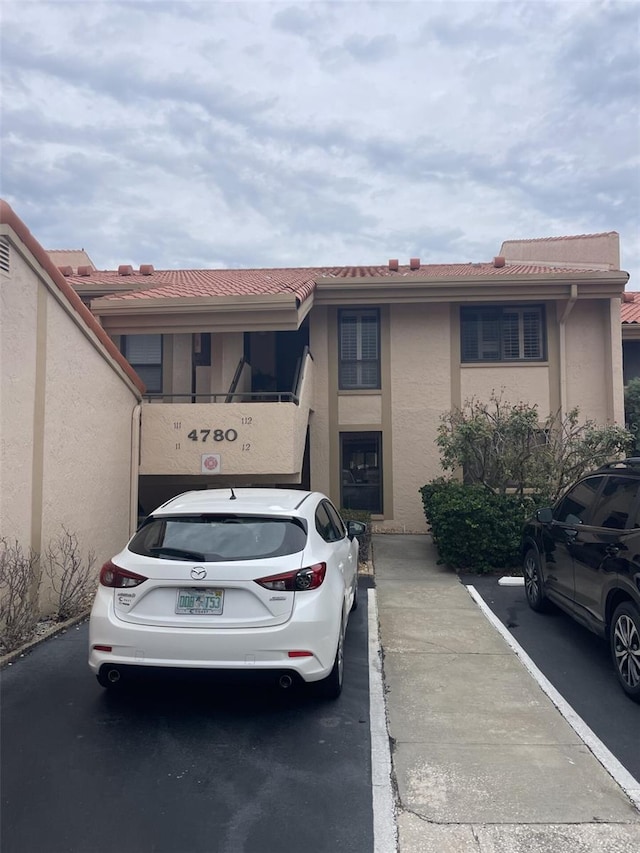 view of property with uncovered parking, a tile roof, and stucco siding