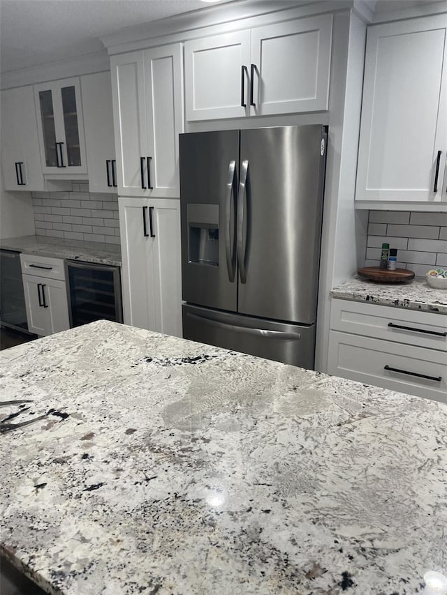 kitchen with tasteful backsplash, glass insert cabinets, light stone countertops, beverage cooler, and stainless steel fridge with ice dispenser