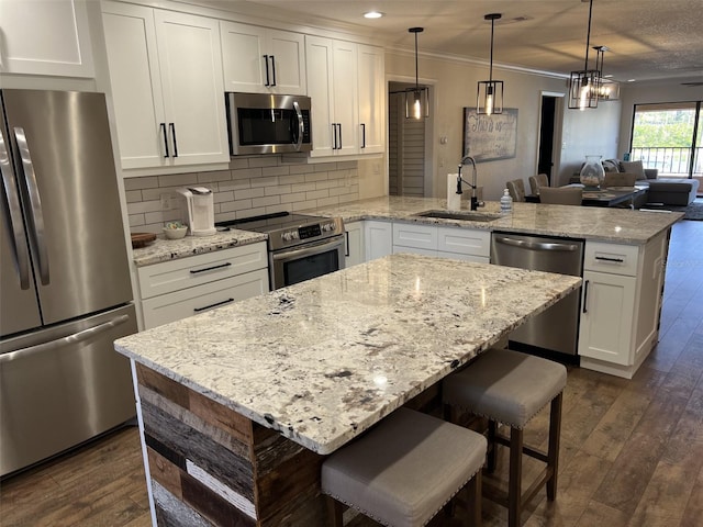 kitchen featuring dark wood finished floors, a peninsula, stainless steel appliances, crown molding, and a sink