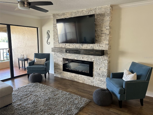 living area featuring ornamental molding, a large fireplace, a textured ceiling, and wood finished floors