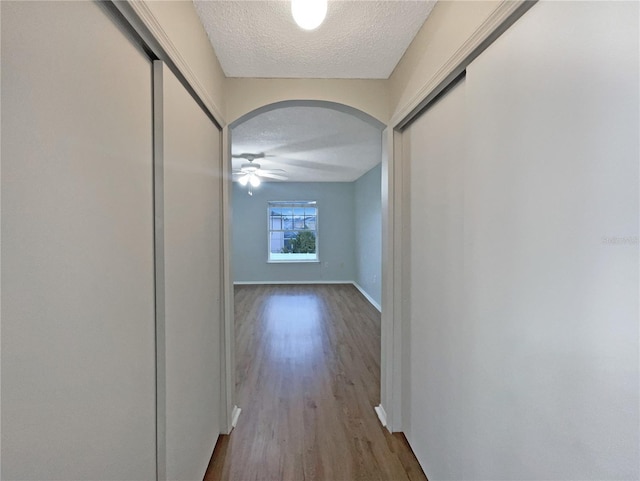 corridor featuring baseboards, arched walkways, a textured ceiling, and wood finished floors