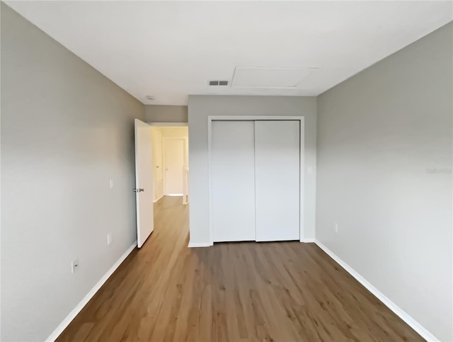 unfurnished bedroom with attic access, baseboards, visible vents, wood finished floors, and a closet