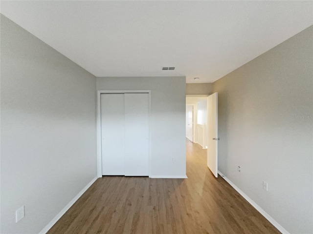 unfurnished bedroom featuring baseboards, a closet, visible vents, and wood finished floors