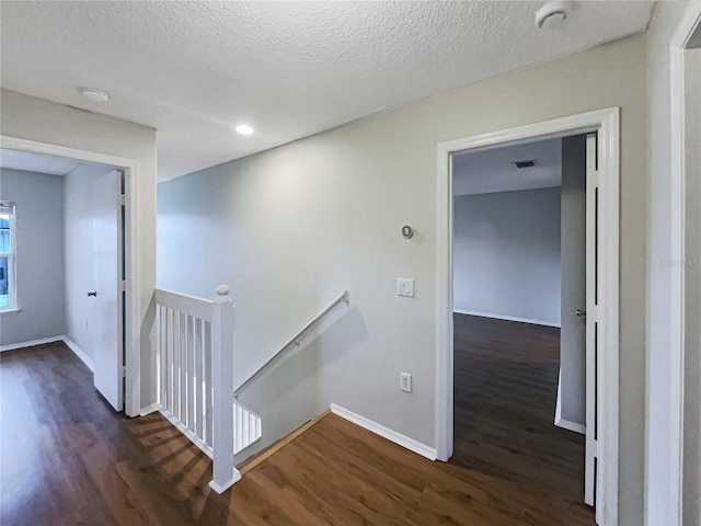 corridor featuring dark wood-style floors, a textured ceiling, an upstairs landing, and baseboards