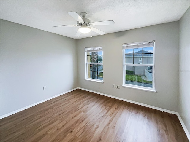 empty room with ceiling fan, a textured ceiling, baseboards, and wood finished floors