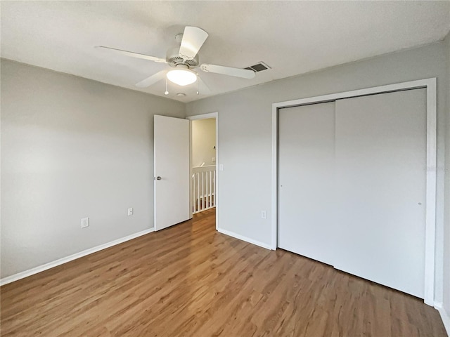 unfurnished bedroom with ceiling fan, wood finished floors, visible vents, baseboards, and a closet