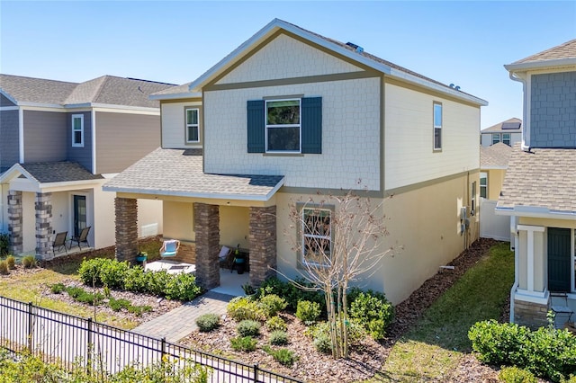 view of front of property with a patio area, roof with shingles, fence, and stucco siding