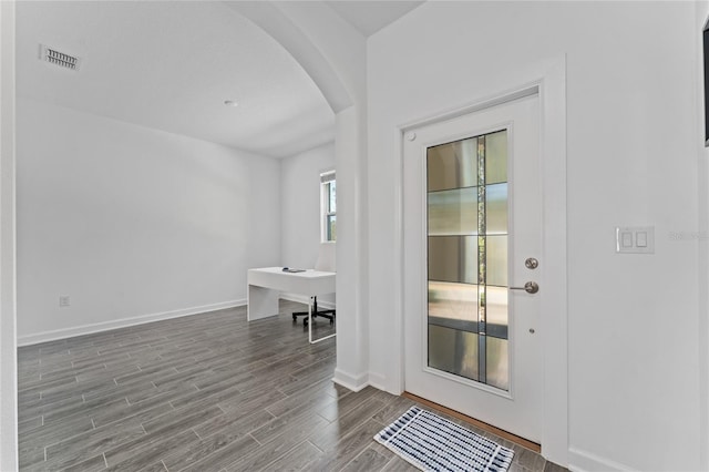 foyer entrance with arched walkways, visible vents, baseboards, and wood finished floors