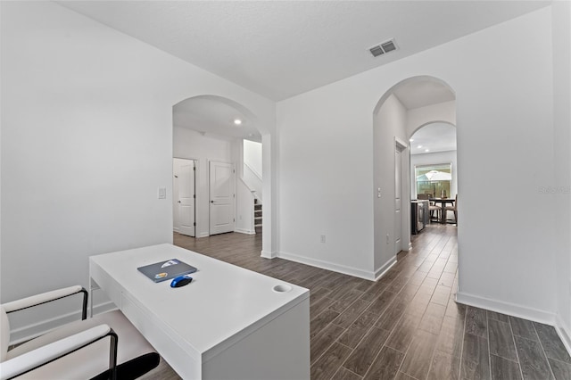 home office with baseboards, visible vents, dark wood finished floors, and arched walkways