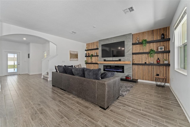 living area with wood finish floors, visible vents, arched walkways, and a tile fireplace