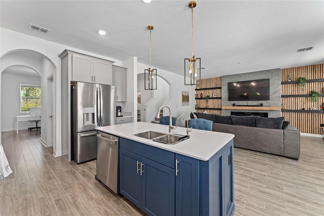 kitchen with blue cabinetry, stainless steel appliances, light countertops, a sink, and an island with sink