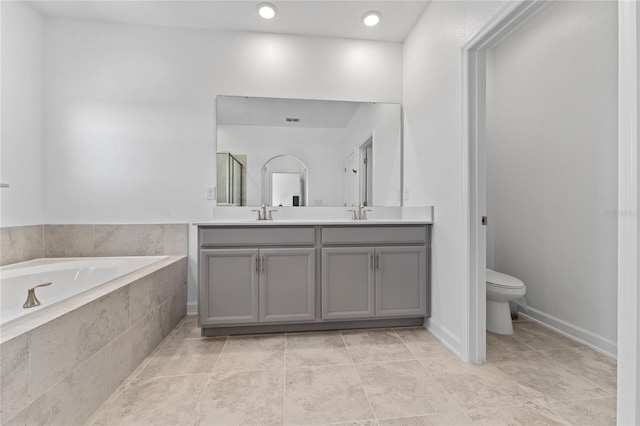 bathroom featuring toilet, a garden tub, double vanity, and a sink