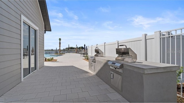 view of patio with a fenced in pool, a water view, grilling area, an outdoor kitchen, and fence