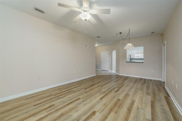 empty room with light wood-style floors, visible vents, a textured ceiling, and baseboards