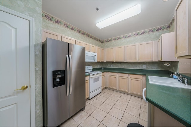 kitchen featuring white appliances, dark countertops, light brown cabinetry, a sink, and light tile patterned flooring