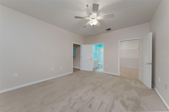 unfurnished bedroom with a walk in closet, a closet, light colored carpet, a textured ceiling, and baseboards