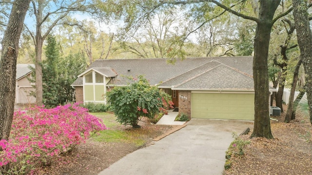 view of front of home featuring roof with shingles, brick siding, central air condition unit, an attached garage, and driveway