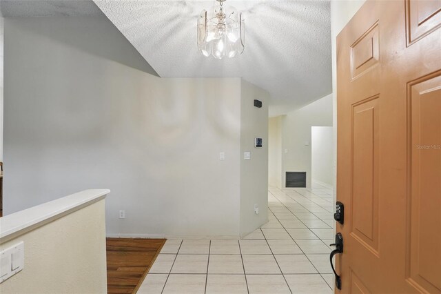 hallway with visible vents, a textured ceiling, an upstairs landing, a chandelier, and light tile patterned flooring