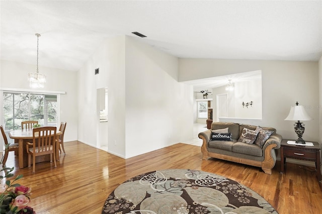 living area with wood finished floors, vaulted ceiling, and an inviting chandelier