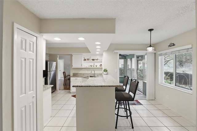 kitchen featuring light tile patterned floors, freestanding refrigerator, a peninsula, open shelves, and a sink