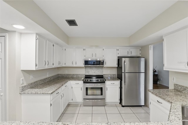 kitchen with light tile patterned floors, light stone counters, stainless steel appliances, visible vents, and white cabinets