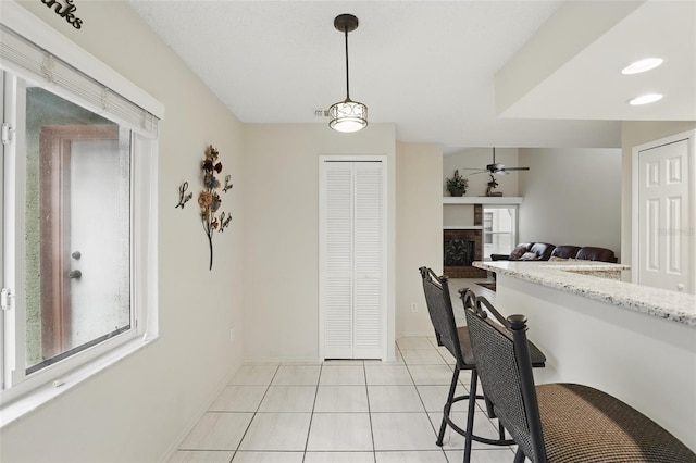 kitchen featuring light stone counters, a fireplace, light tile patterned floors, hanging light fixtures, and ceiling fan