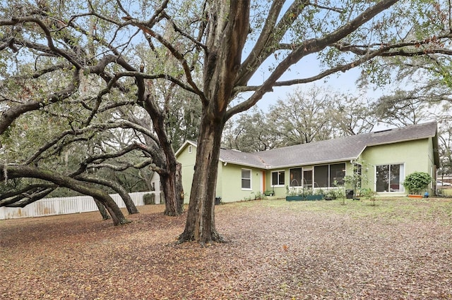 rear view of house featuring fence, a sunroom, and stucco siding