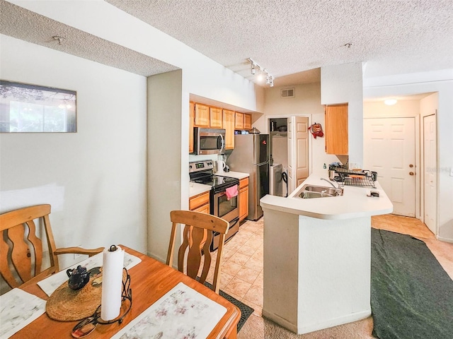 kitchen with visible vents, a peninsula, stainless steel appliances, a textured ceiling, and a sink