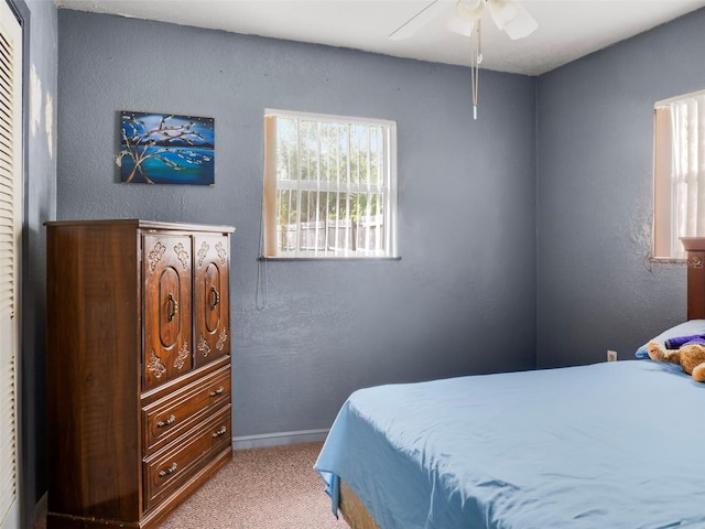 carpeted bedroom with a textured wall, baseboards, and ceiling fan