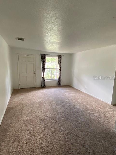 carpeted spare room featuring visible vents and a textured ceiling