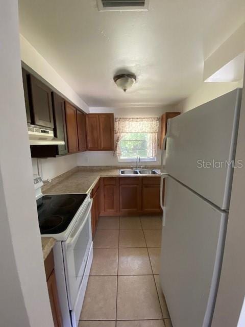 kitchen with white appliances, under cabinet range hood, light countertops, and a sink