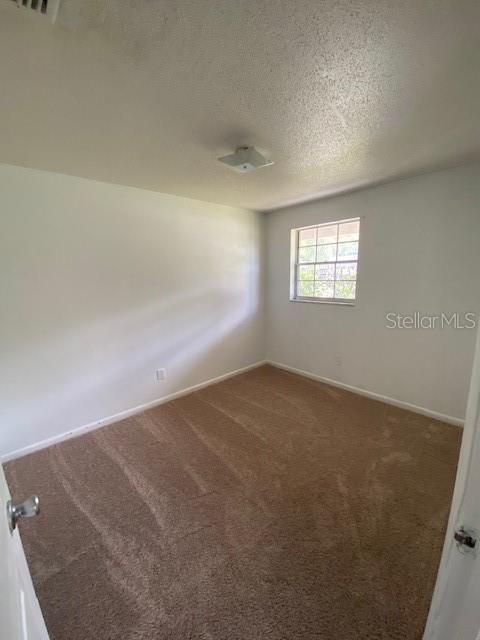 empty room featuring dark carpet, a textured ceiling, and baseboards